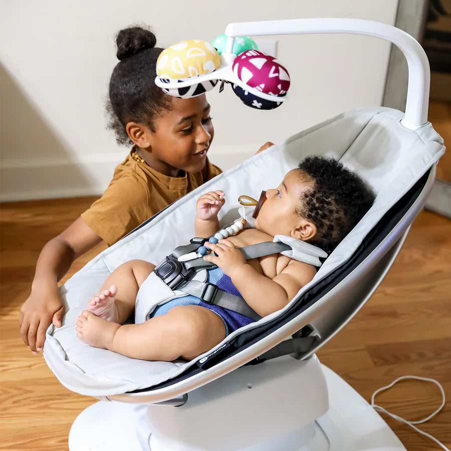 baby playing in Grey MamaRoo Multi-Motion Baby Swing featuring a machine-washable seat cover, removable toy bar, and app compatibility for customizable motions and sounds