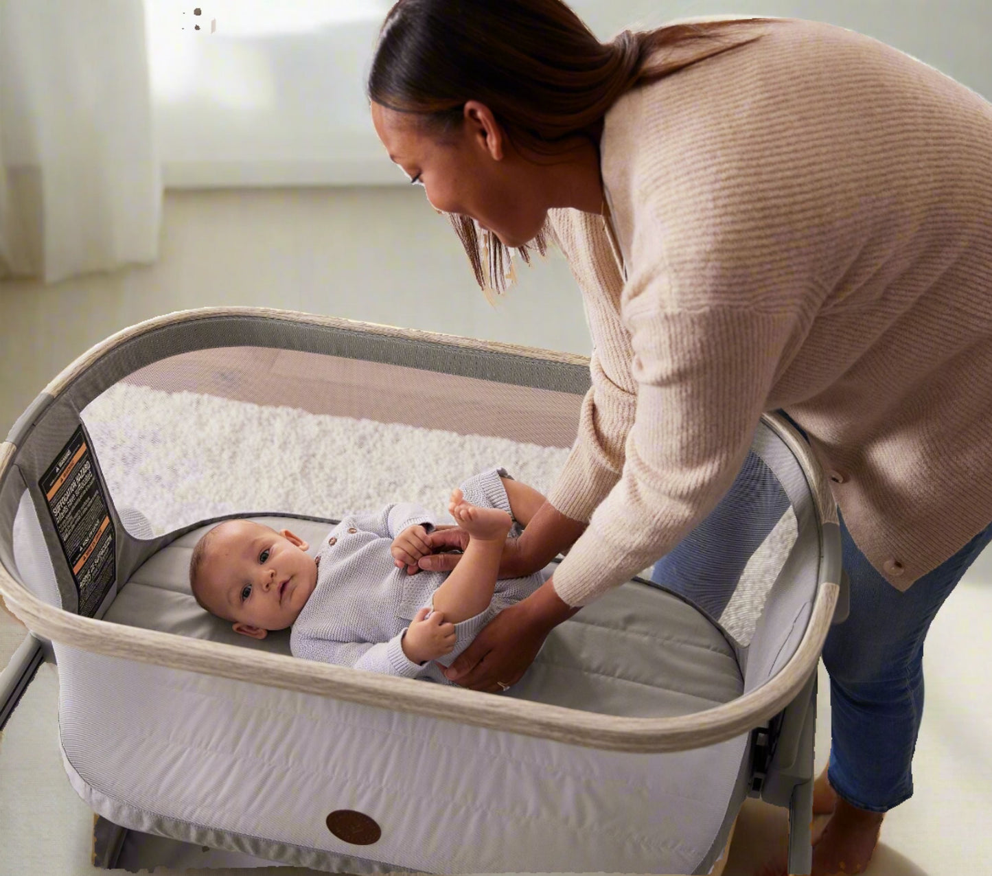 Mother placing her baby in the Maxi-Cosi® Iora Newborn Bassinet, highlighting the bassinet's spacious and comfortable sleeping area.